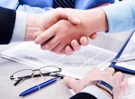 Close Up Of Business Handshake Over Workplace With Documents, Pens, Glasses